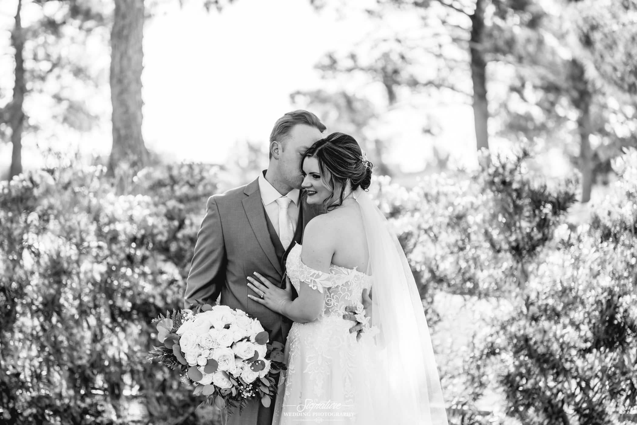 Groom kissing bride on cheek black and white