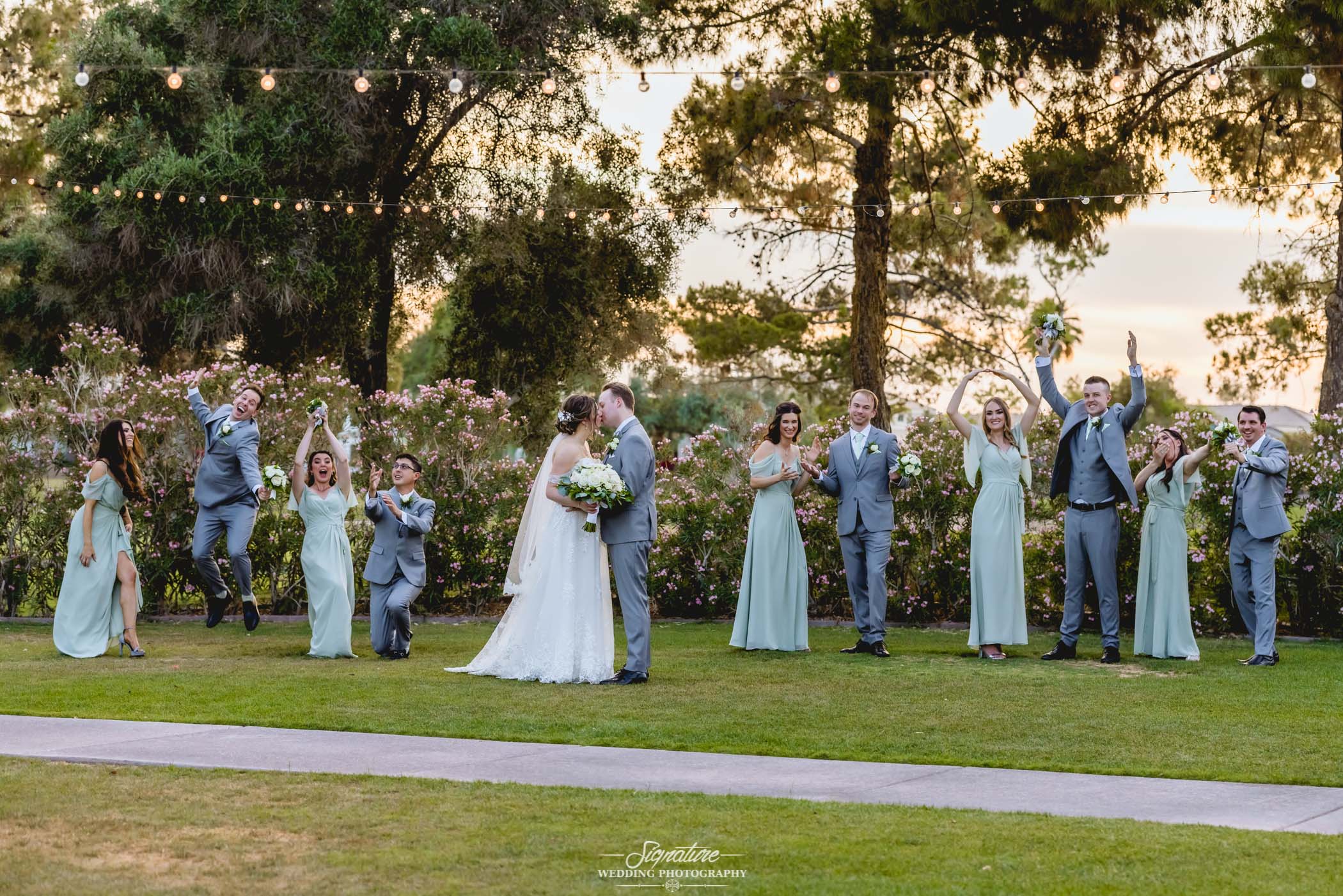 Bride and groom kissing while wedding party does funny poses