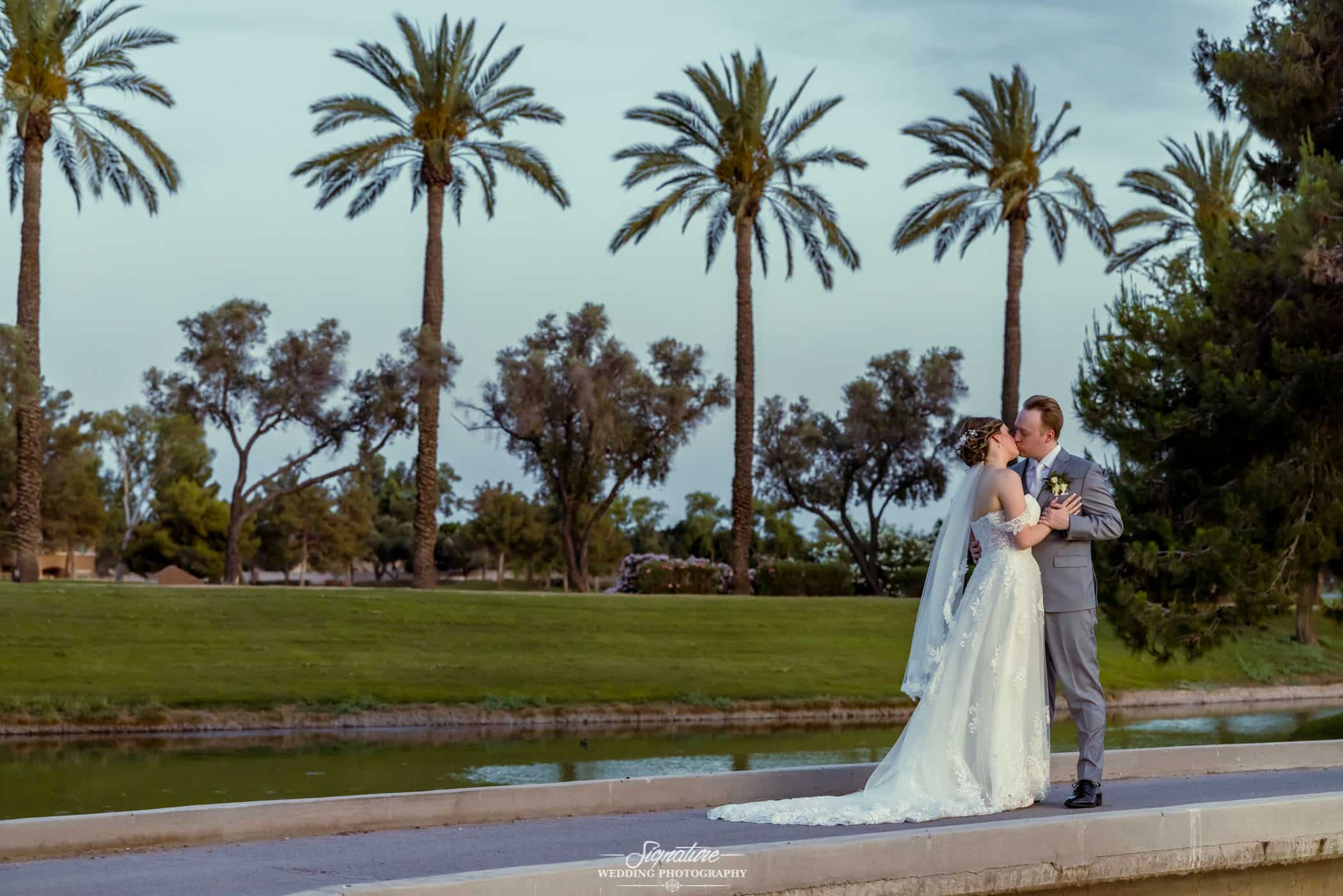 Bride and groom kissing in front of pond and palm trees