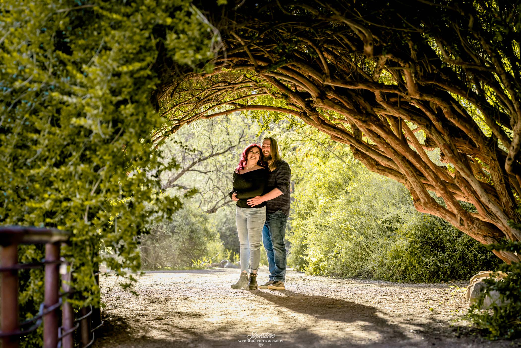 Man holding woman's waist smiling at camera under branch archway