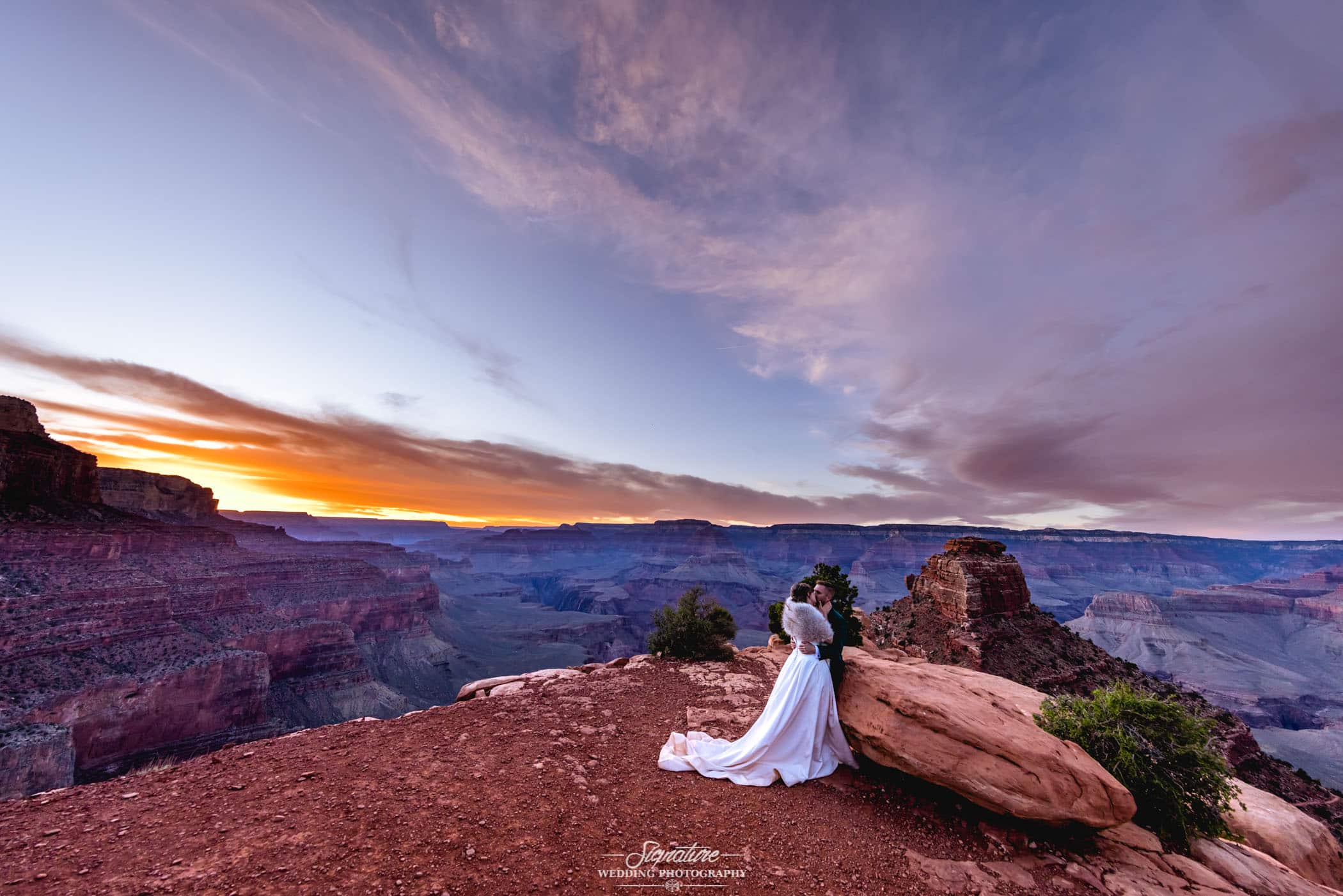 Bride and groom kissing on desert mountain top at sunset