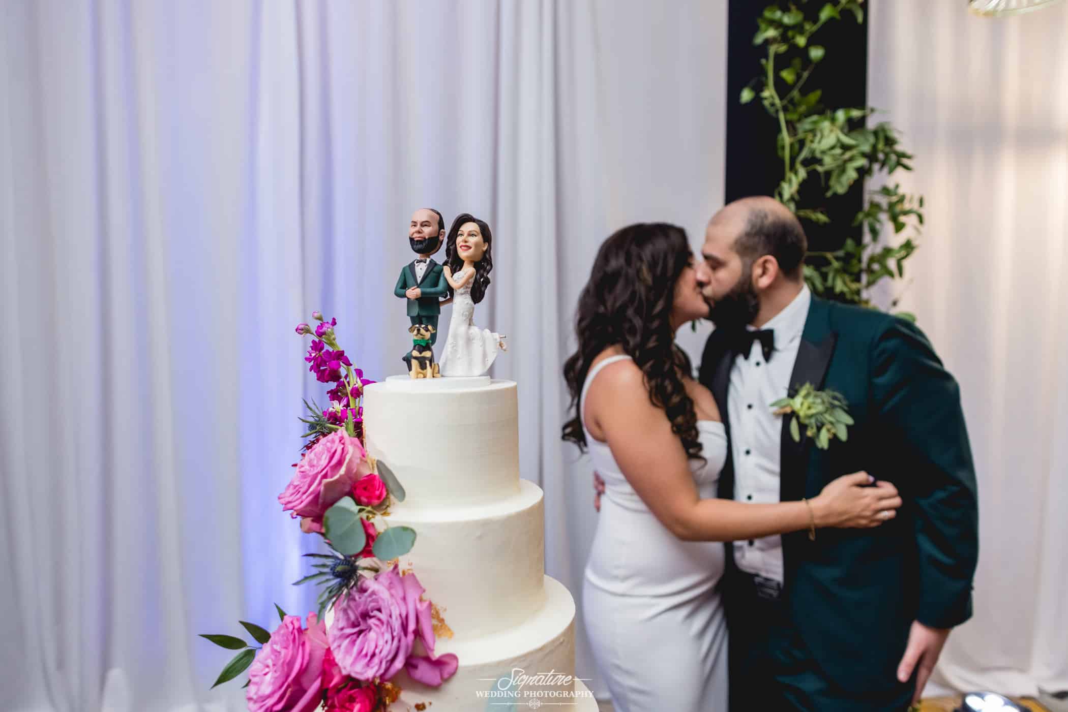 Bride and groom kissing next to wedding cake