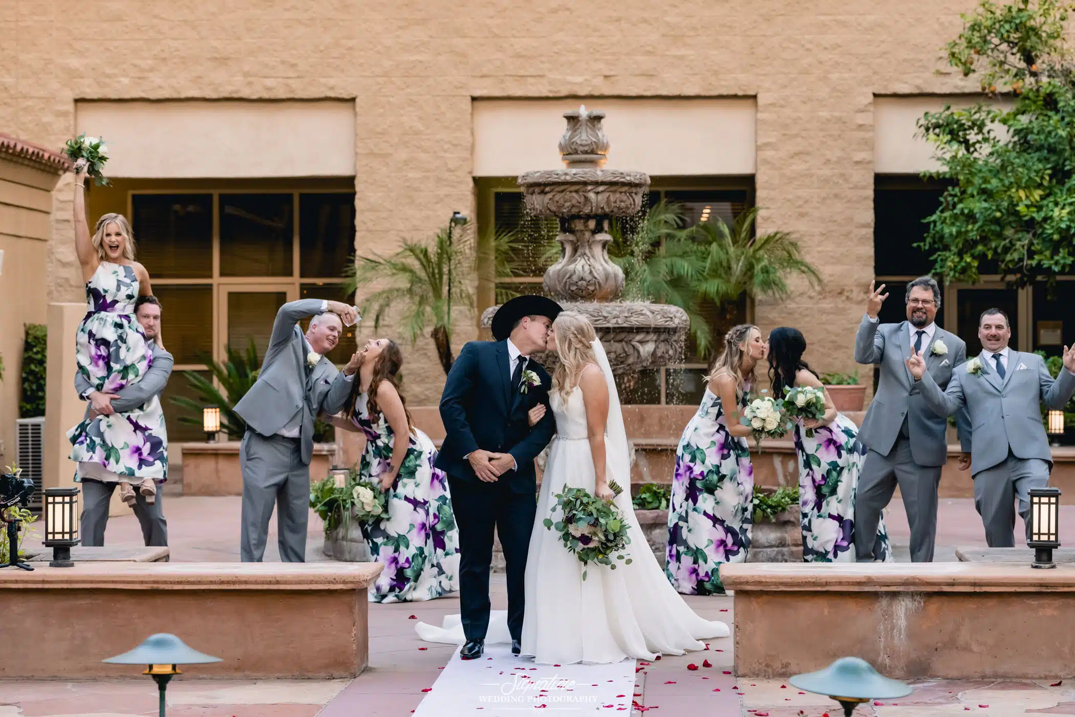 Bride and groom kissing in front of wedding party doing funny pose