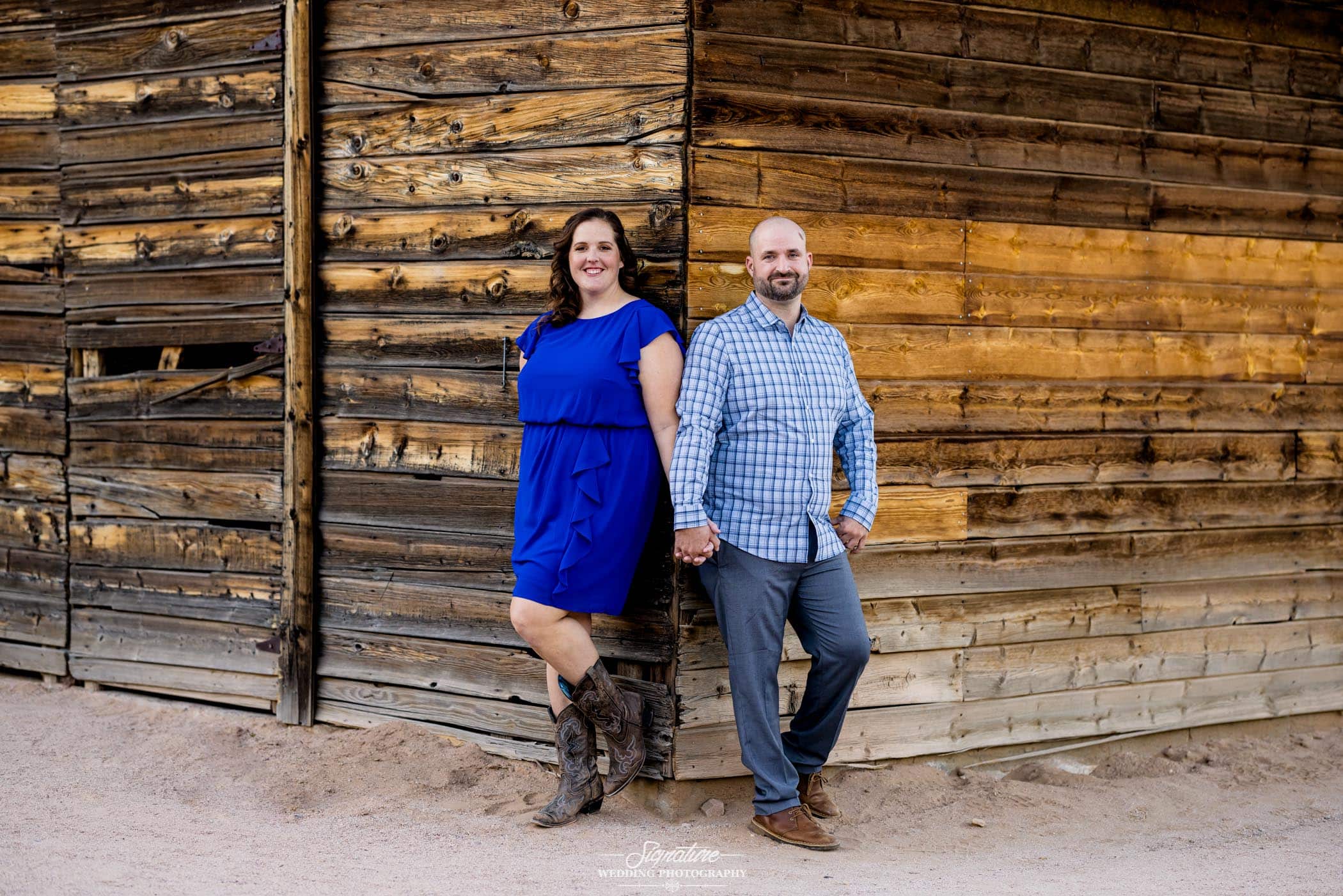 Couple holding hands around corner of wooden barn