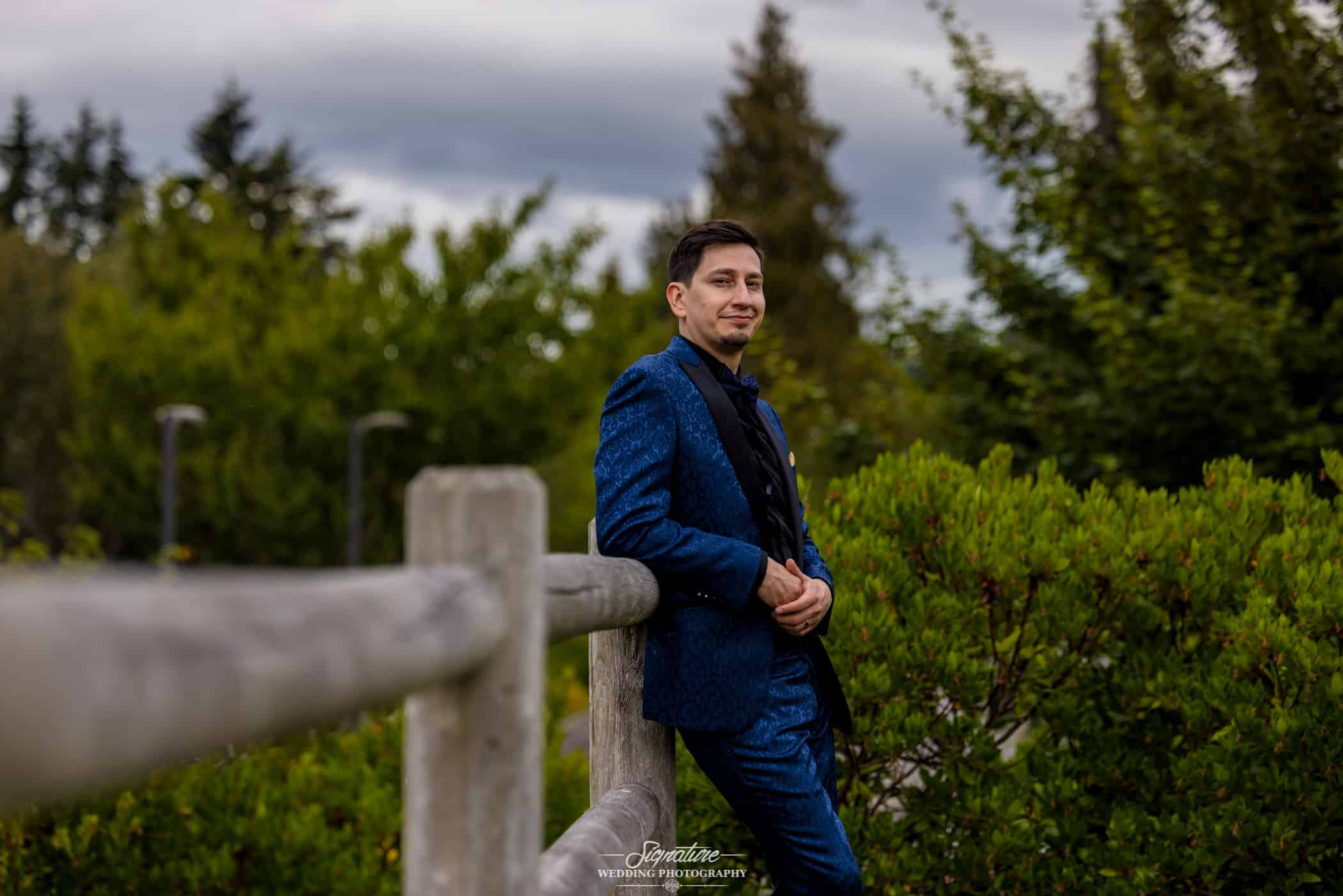 Groom leaning against wood fence