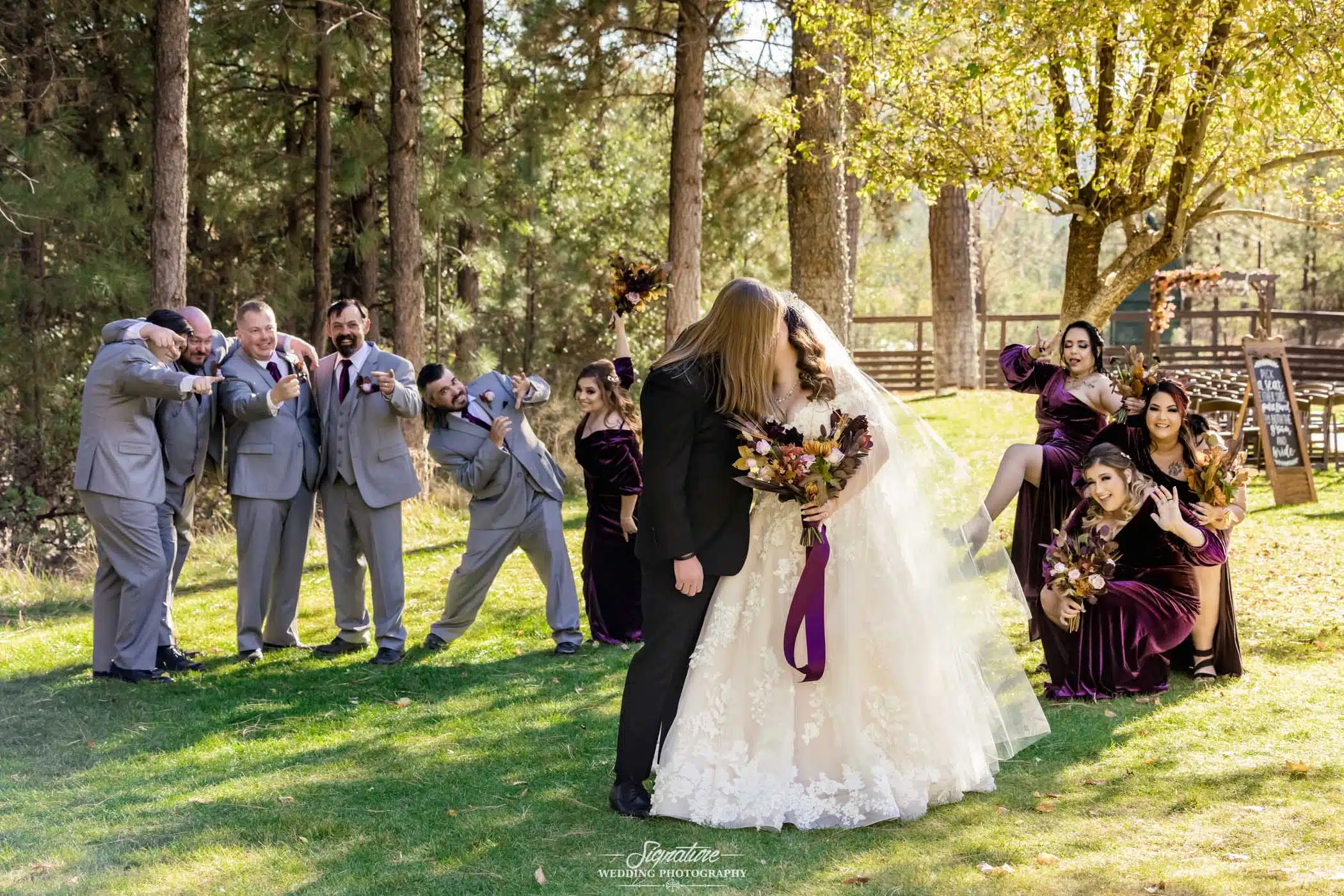 Bride and groom kissing in front of wedding party doing funny pose