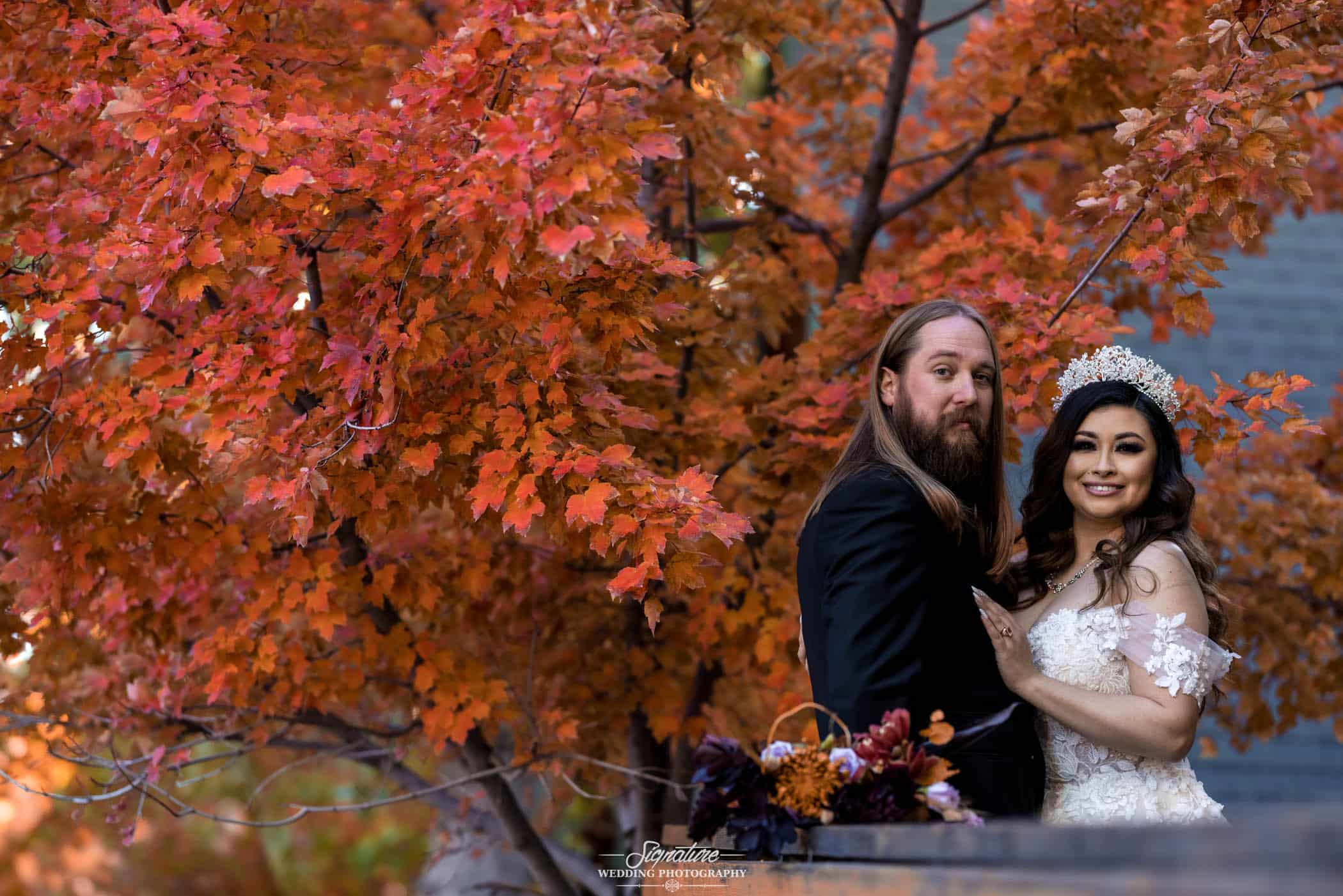 Bride and groom standing in front of fall tree