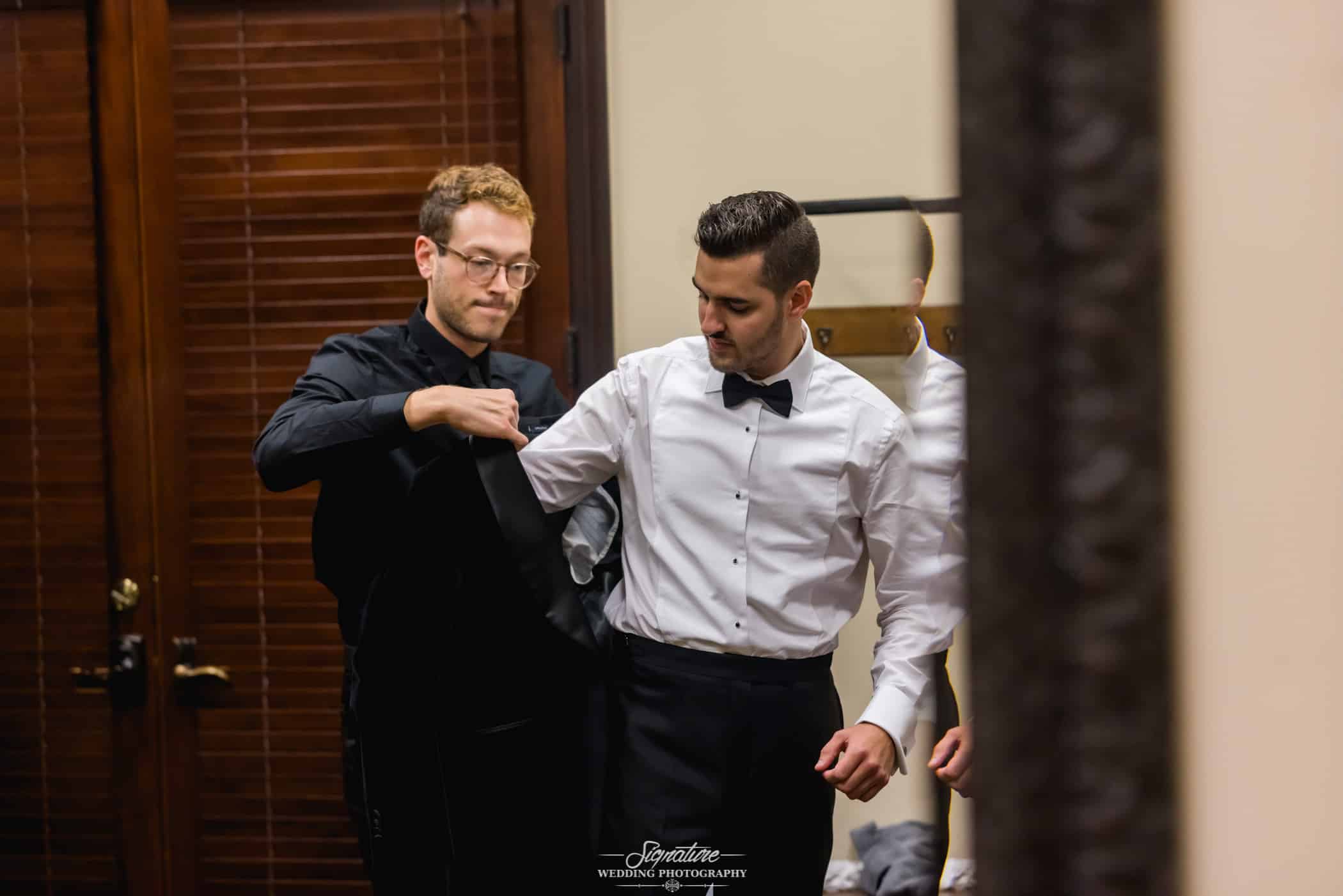 Groomsmen helping groom with jacket