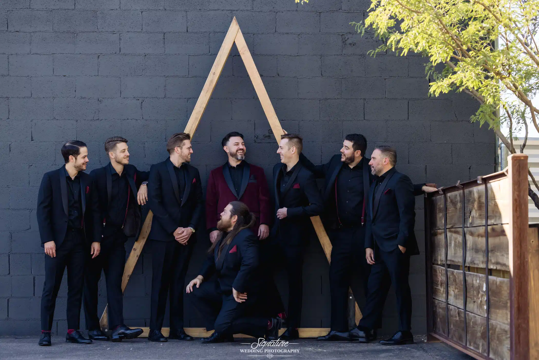 Groom and groomsmen standing against wall smiling