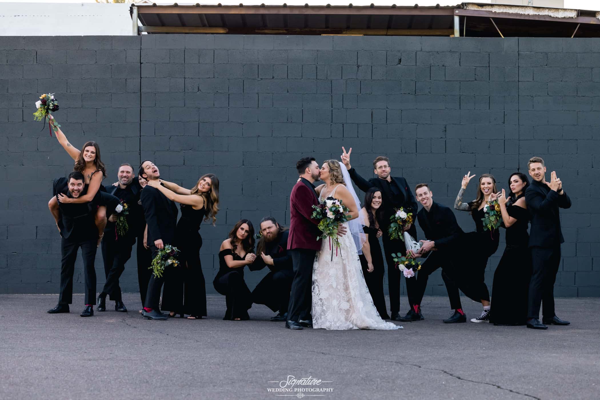 Bride and groom kissing in front of wedding party doing fun pose