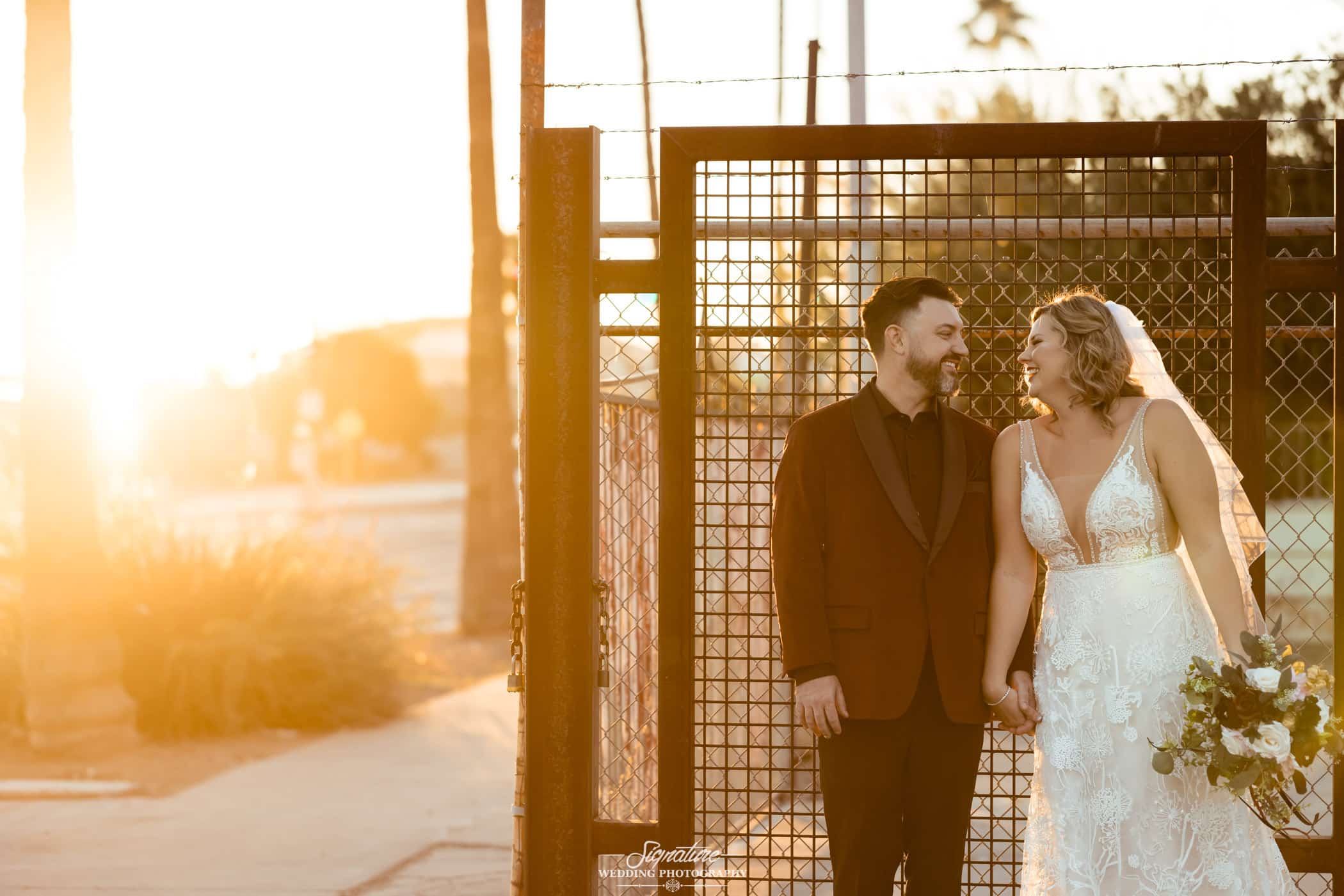 Bride and groom smiling at each other in front of fence