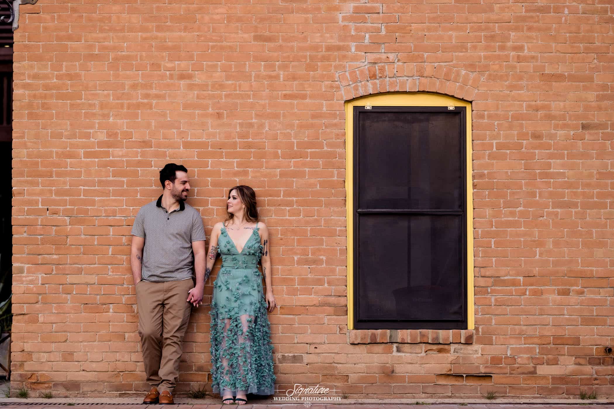 Couple holding hands with back on brick wall