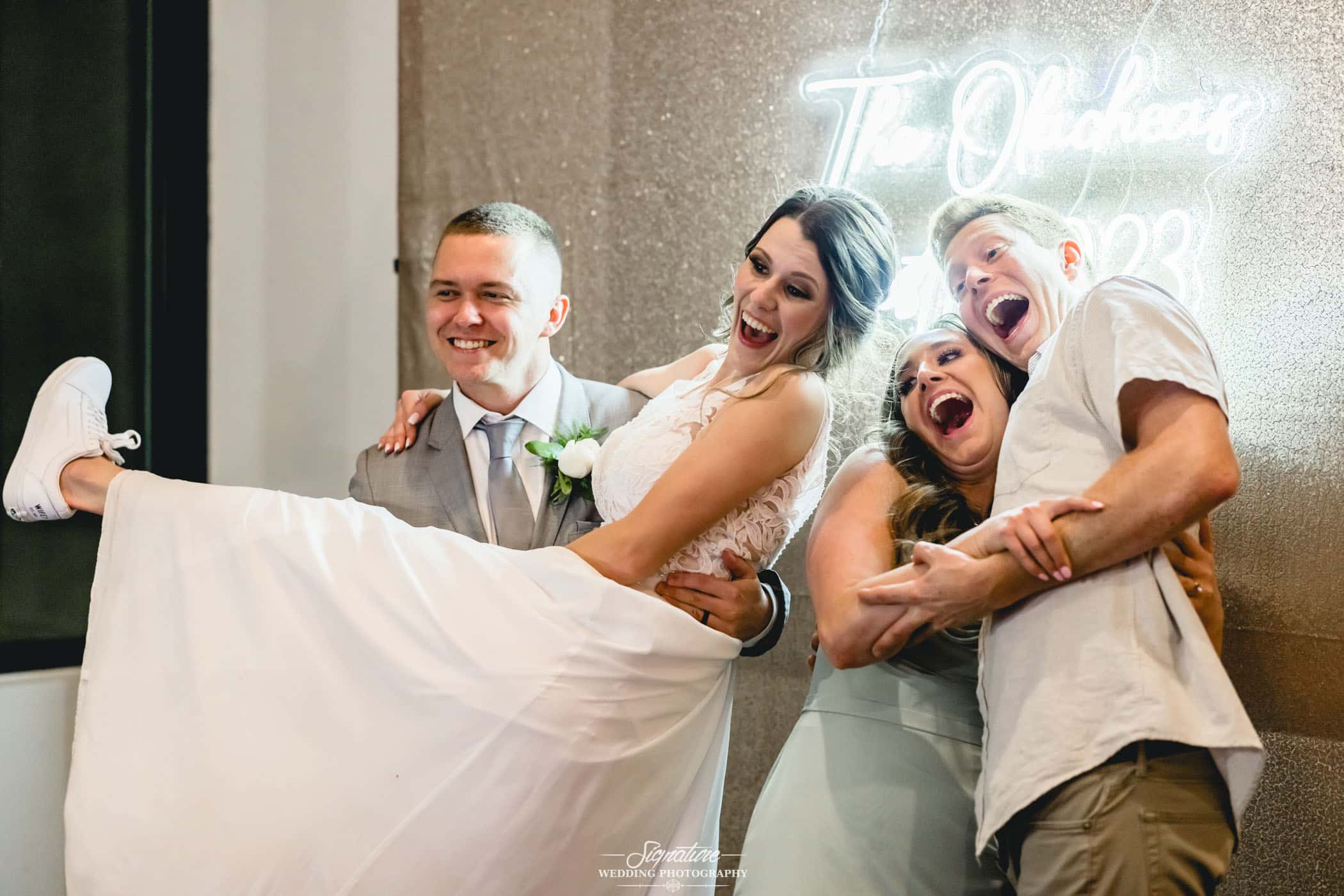 Groom holding bride with wedding guests for photo booth