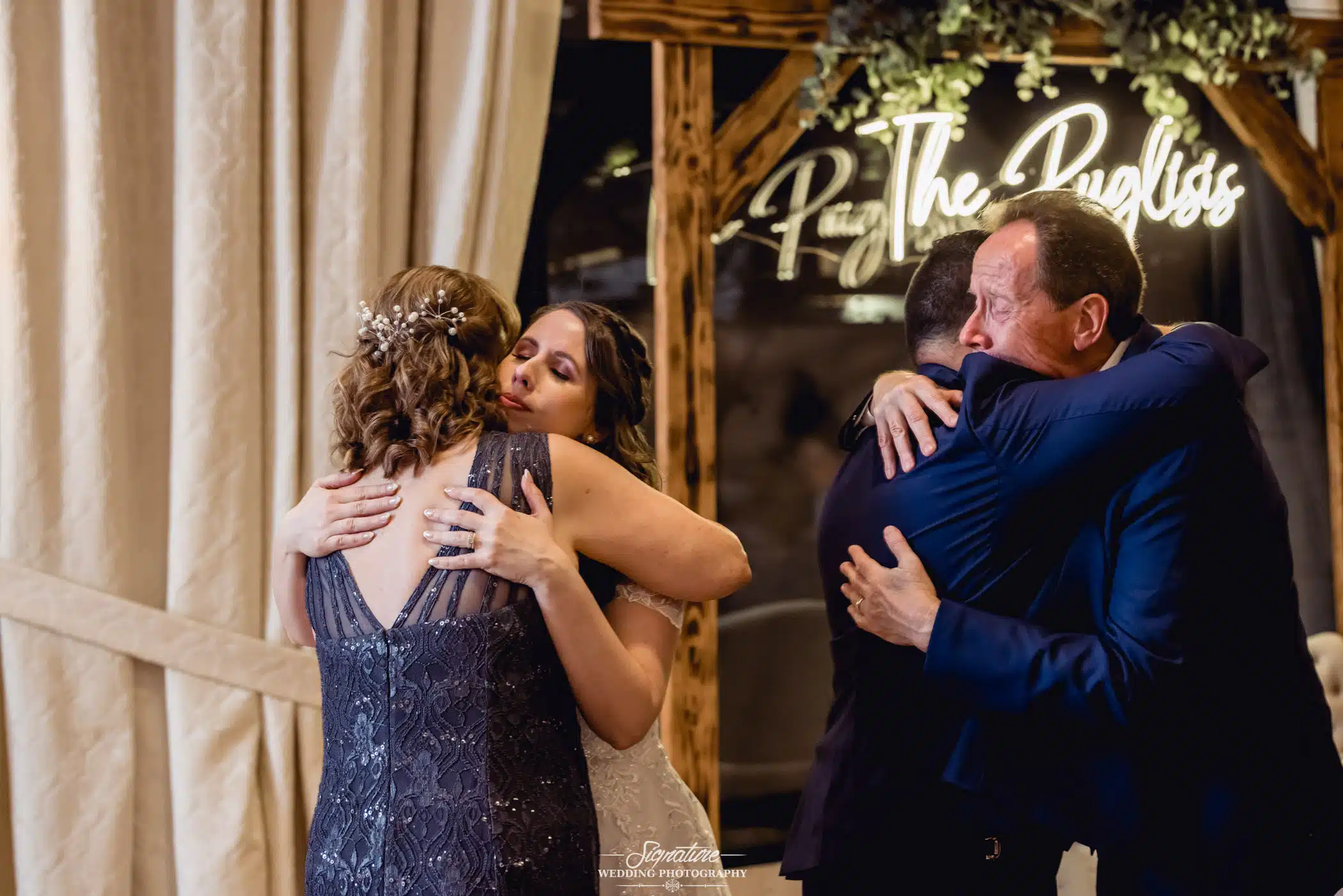 Image by Signature Wedding Photography Bride and groom hugging family