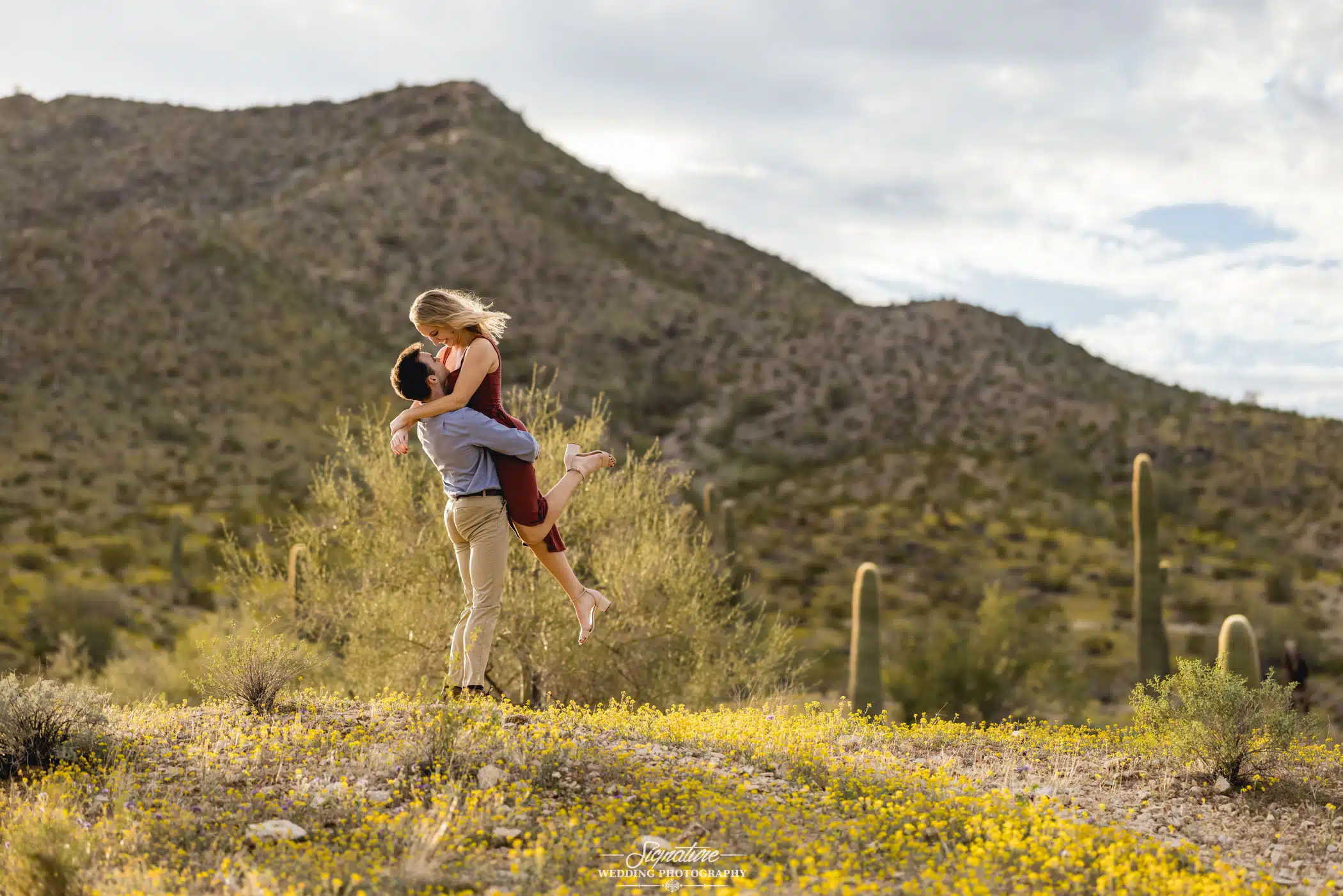Image by Signature Wedding Photography Man picks up woman in front of desert mountain
