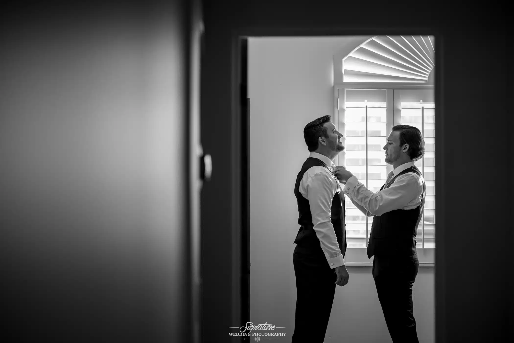 Image by Signature Wedding Photography best man helping the groom with his tie