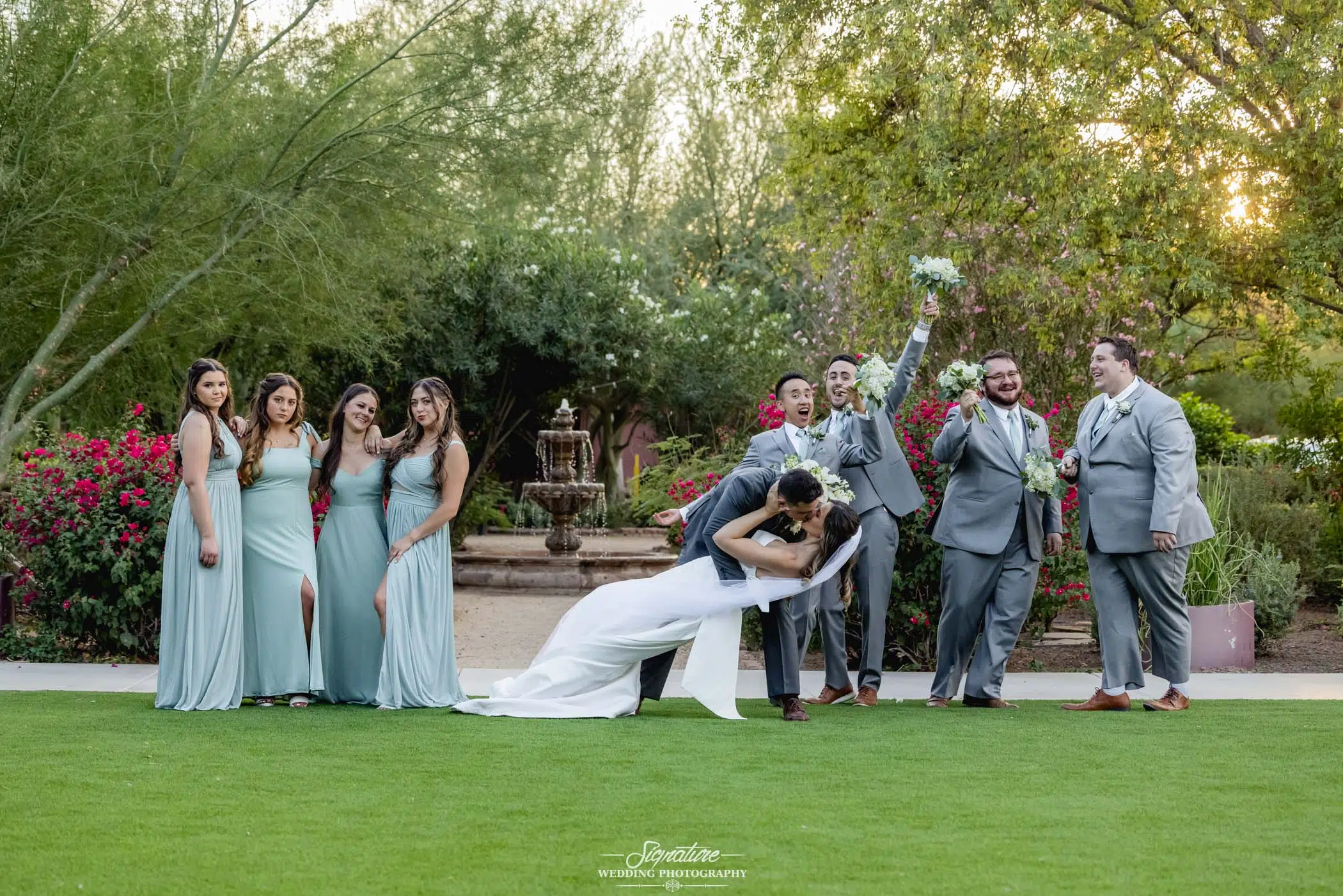 Image by Signature Wedding Photography groom kissing bride with wedding party reacting