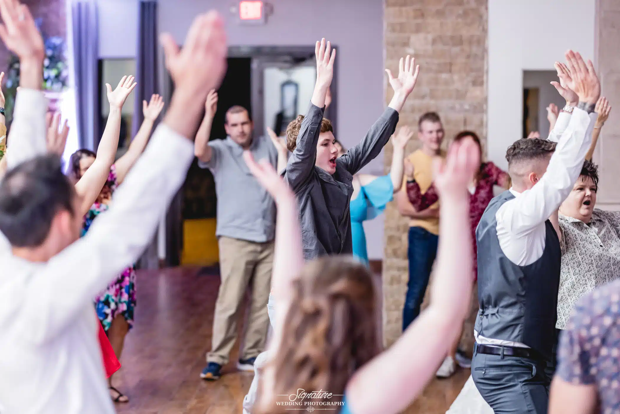 Image by Signature Wedding Photography group of people with their arms up at a wedding reception