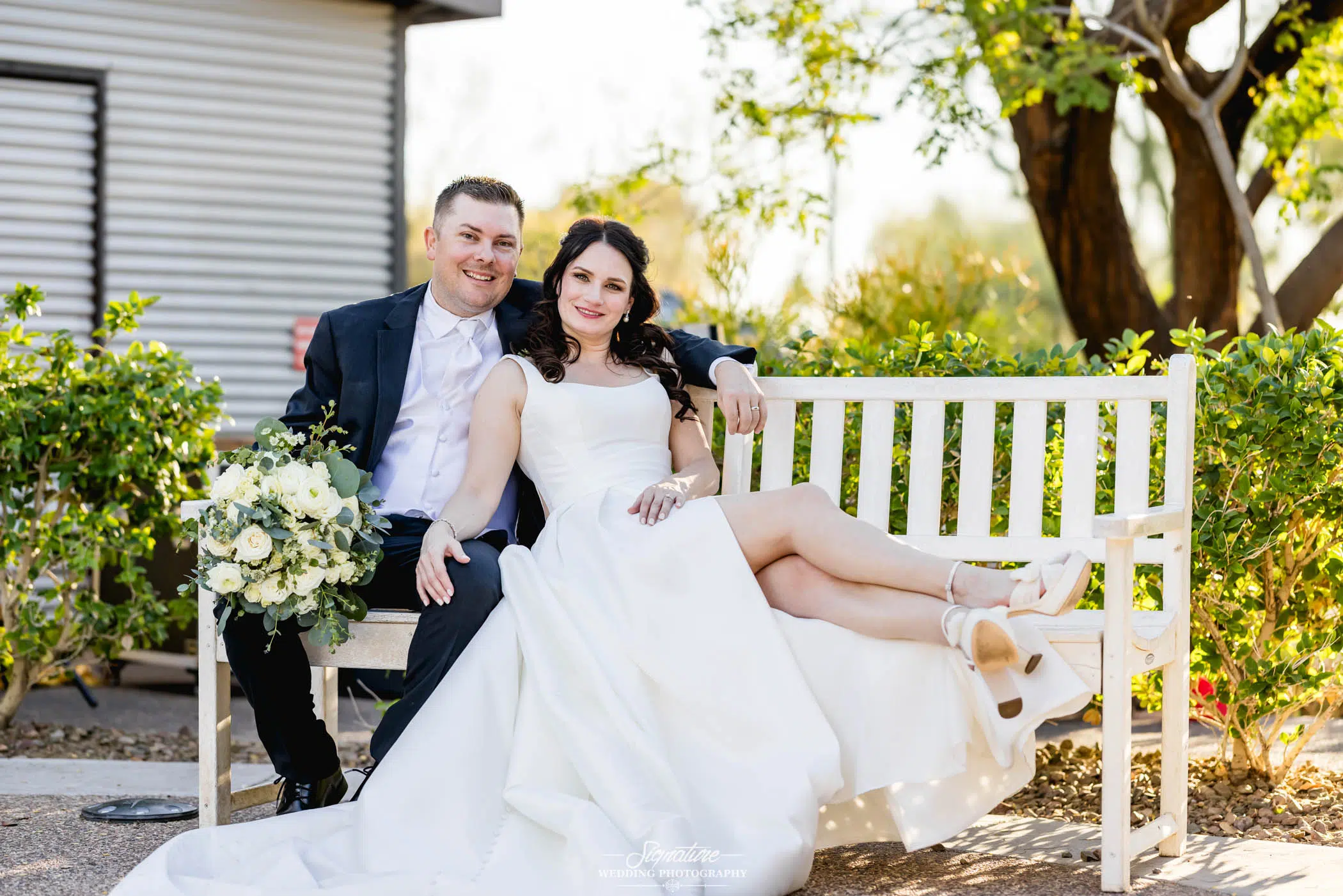Happy newlyweds sitting on a bench together with the brides legs on the bench